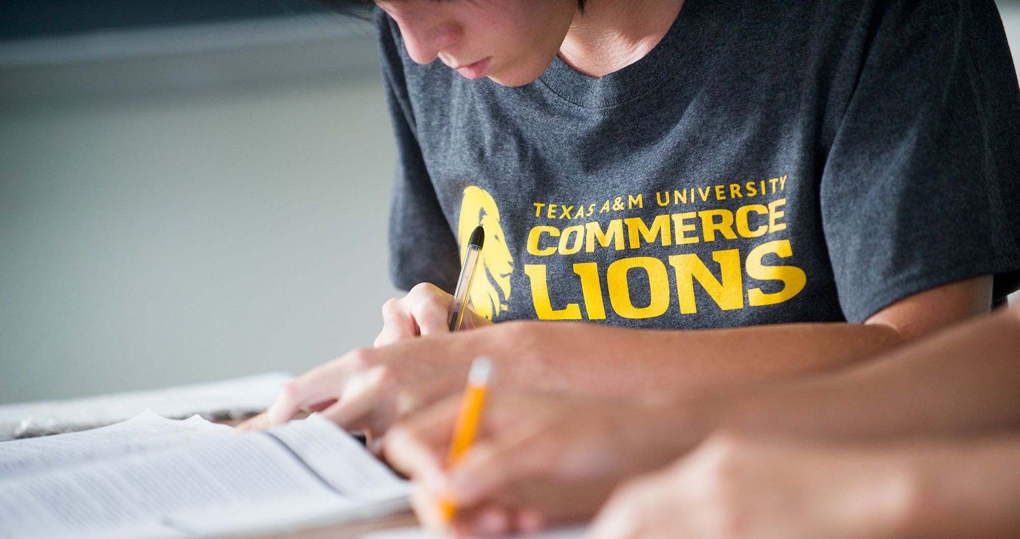 A student completing work wearing a A&M-Commerce t-shirt.