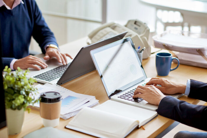 two individual working on laptops sitting at a table facing each other.