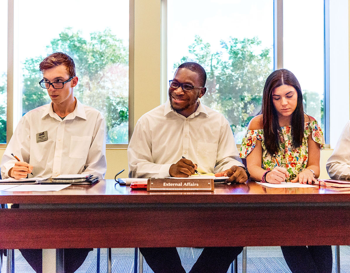 Two male students and one female student sitting at a table during a student government meeting.