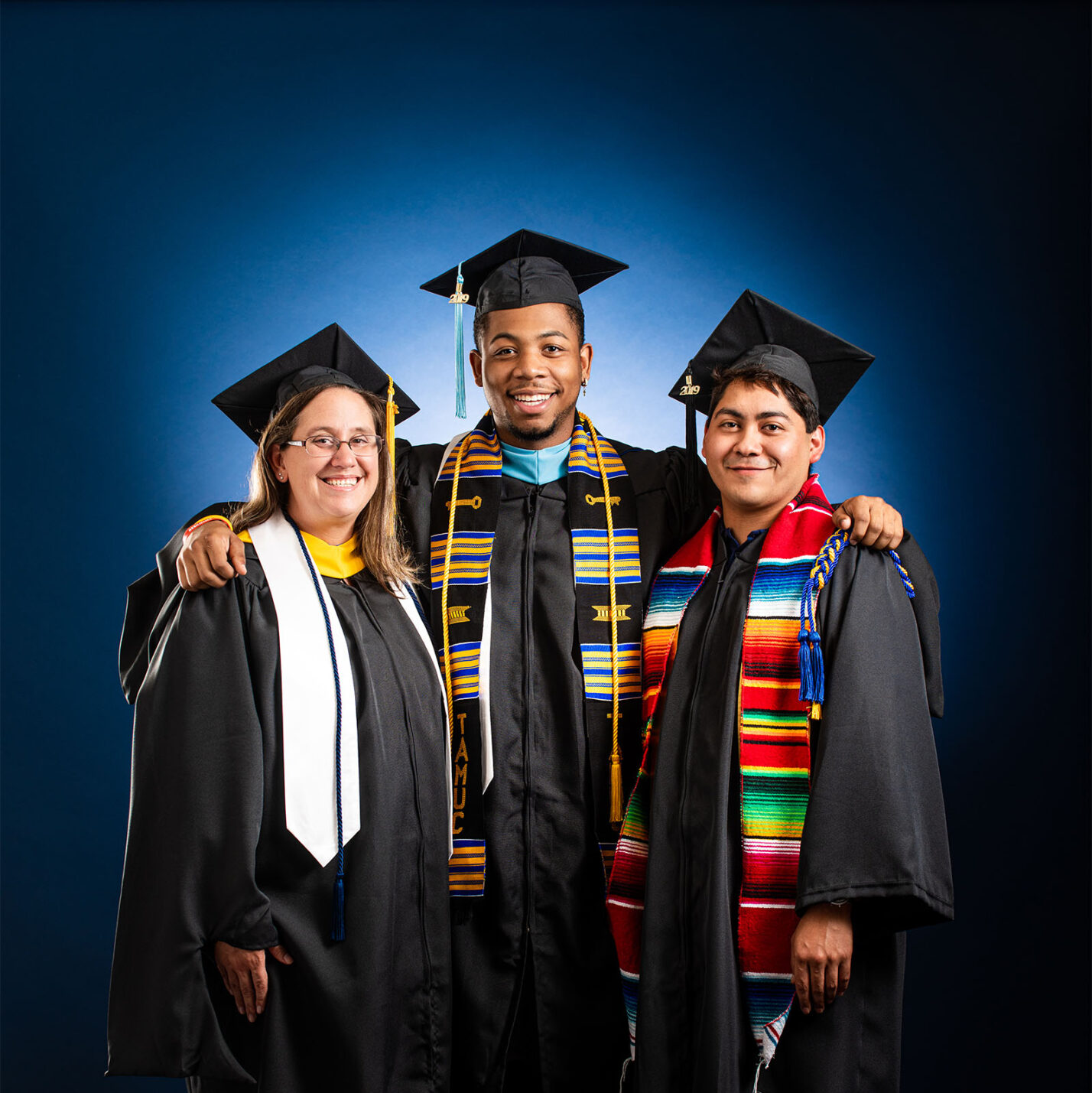 three students smiling at the camera in their cap and gown. 