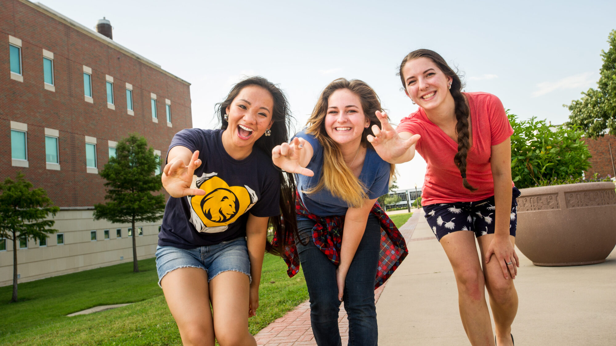 Three female students smiling at the camera and making the lion sign.