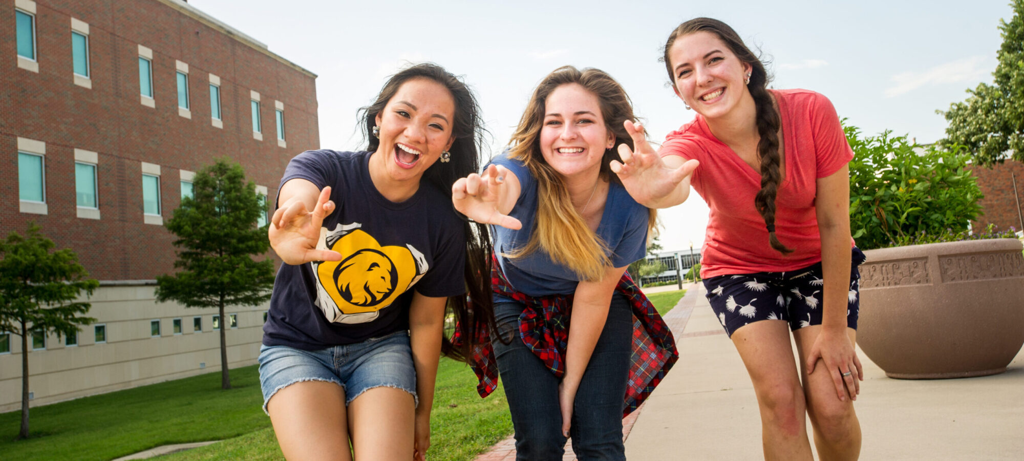 Three female students smiling at the camera making the lions hand sign.
