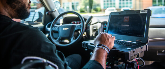 Police officer inside police car looking at the computer.