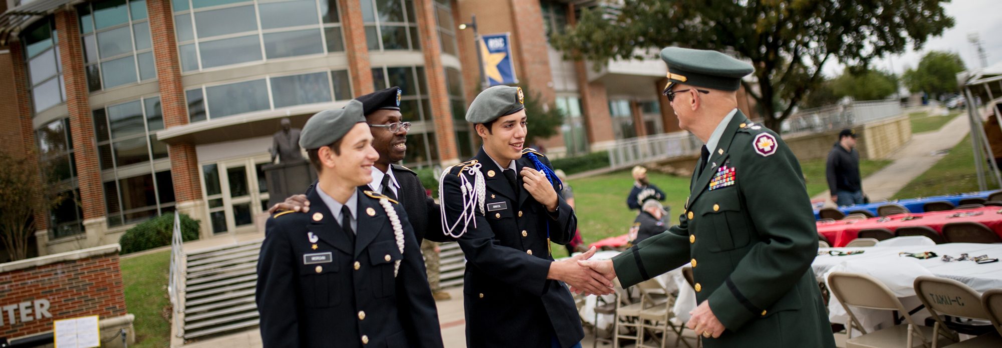 Two young army dressing males are handshaking a male veteran