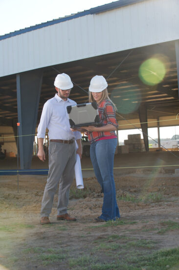 A male and female wearing plastic caps looking at a laptop in front of a building