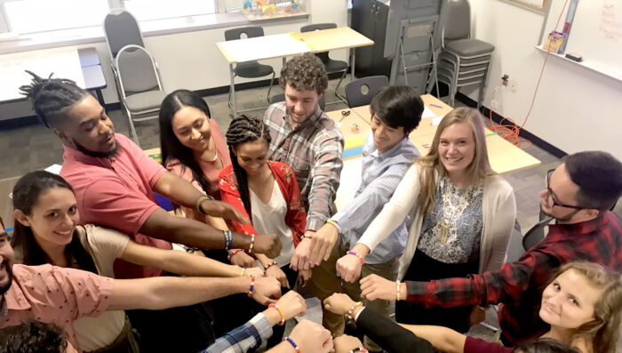 A group of student in a circle touching hands.