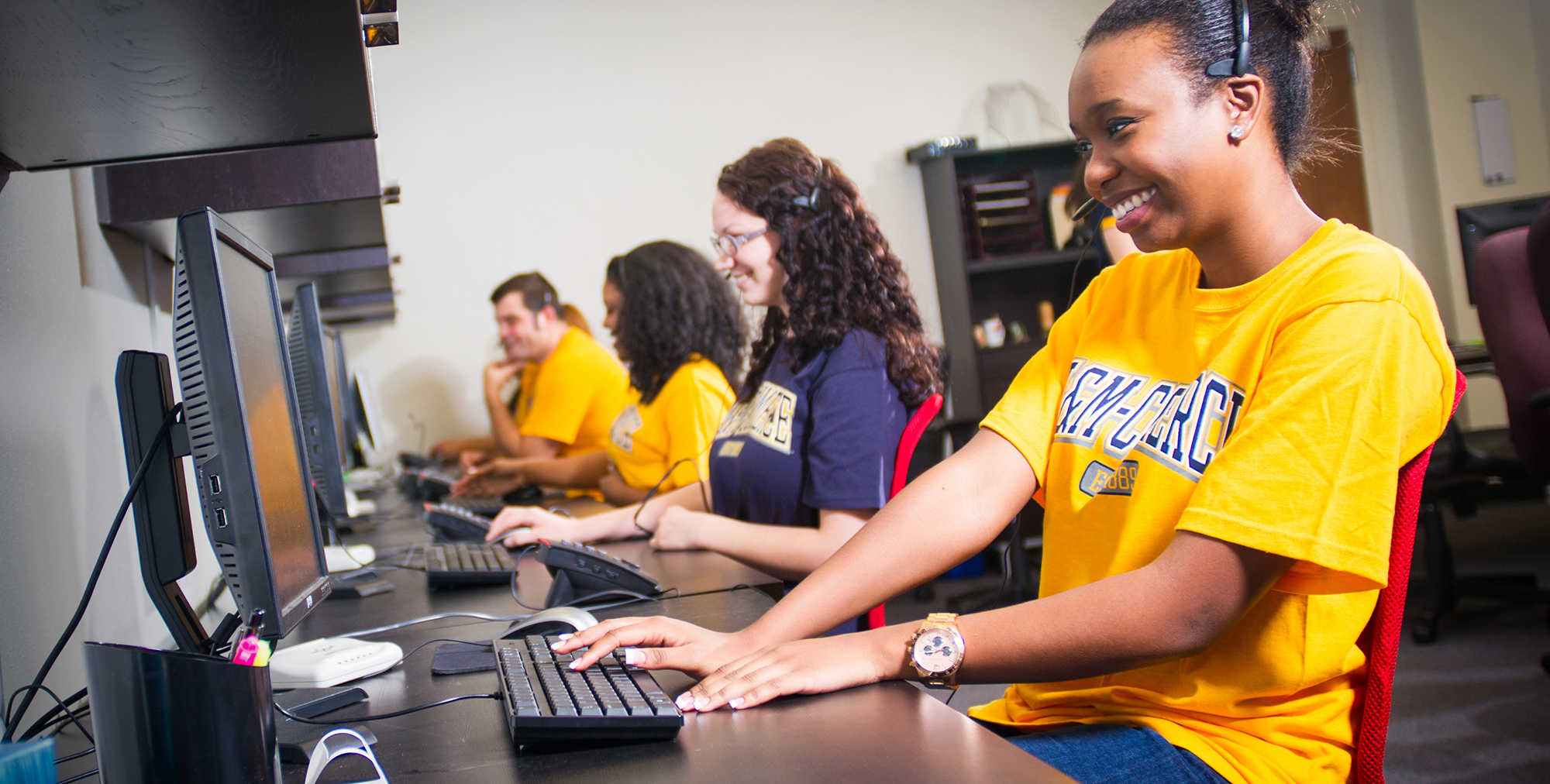 Students employees working happily at computers wearing headphones with a microphone.