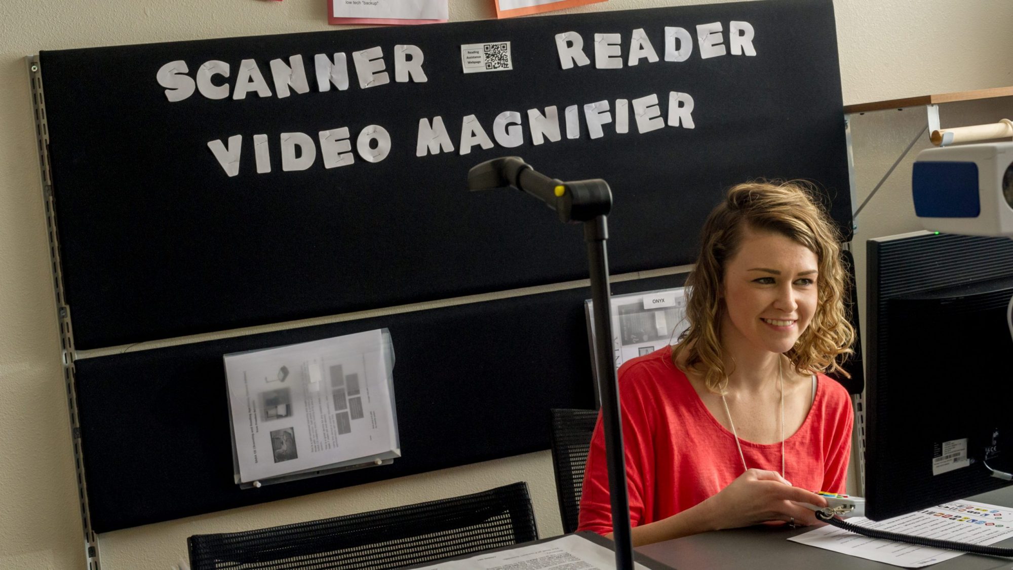 A female student in front of a sign that says scanner reader video magnifier.