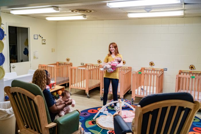 Infant room with two employees holding and playing with infants.