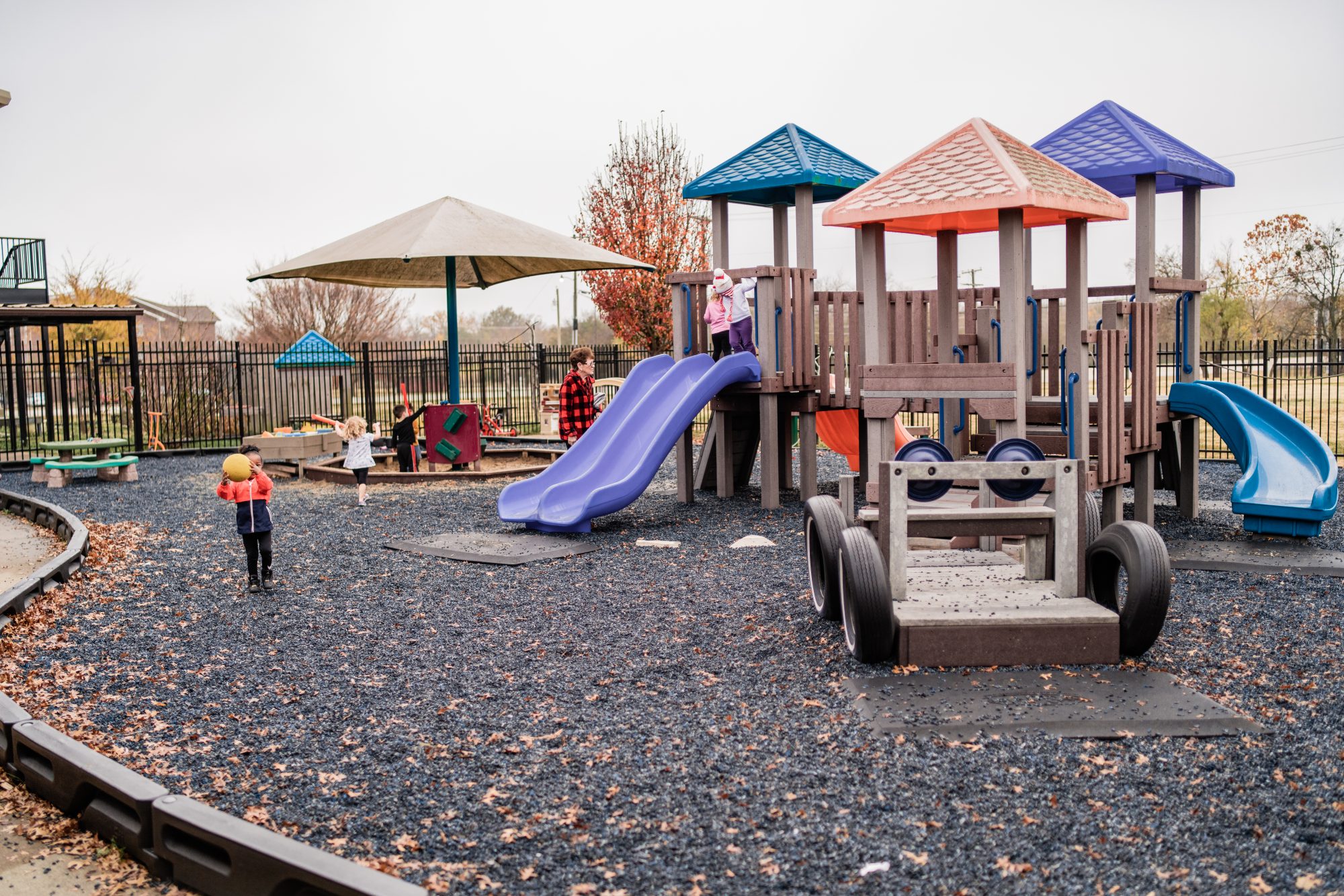 Playground equipment with several slides, swings, sand pit, tricycles and rubber mulch.