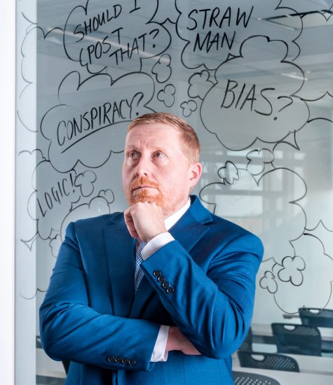 A professor stands pondering in front of glass whiteboard