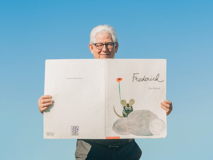 A professor stands holding an oversized copy of the book Frederick