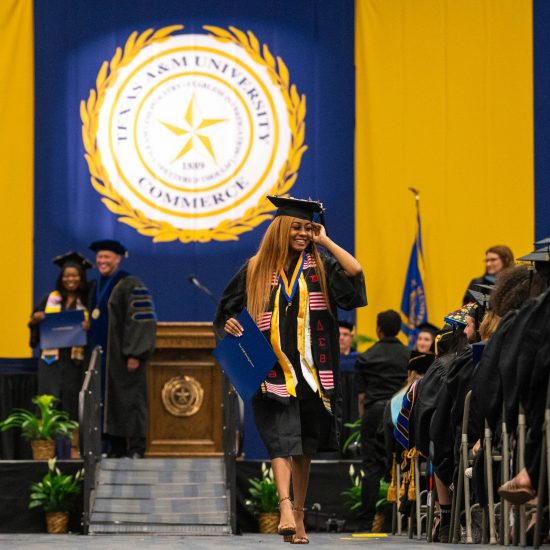 A female student walking down the graduation ceremony smiling.