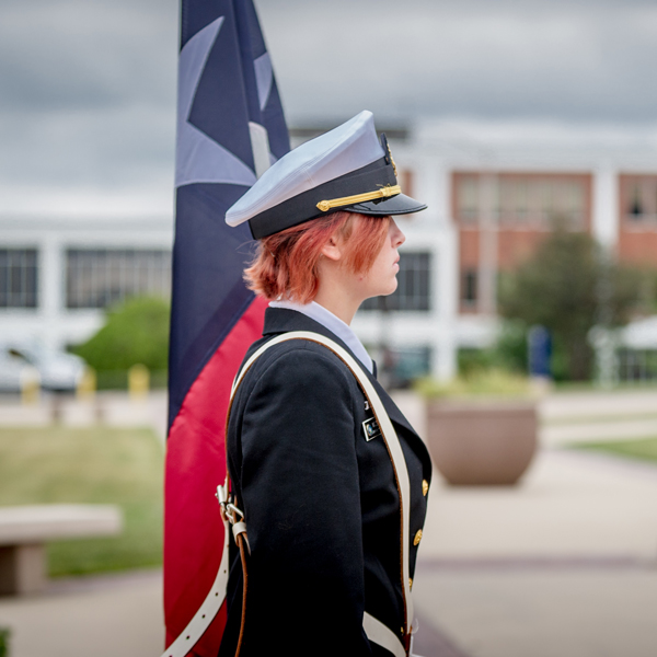 A female soldier standing to the right with a flag beside her.