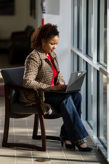 A professional sits near a window with their laptop