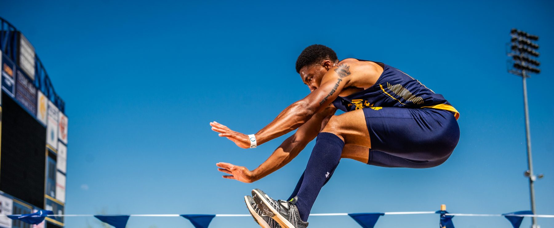 A track and field athlete is depicted in mid-air over a long-jump sand pit.