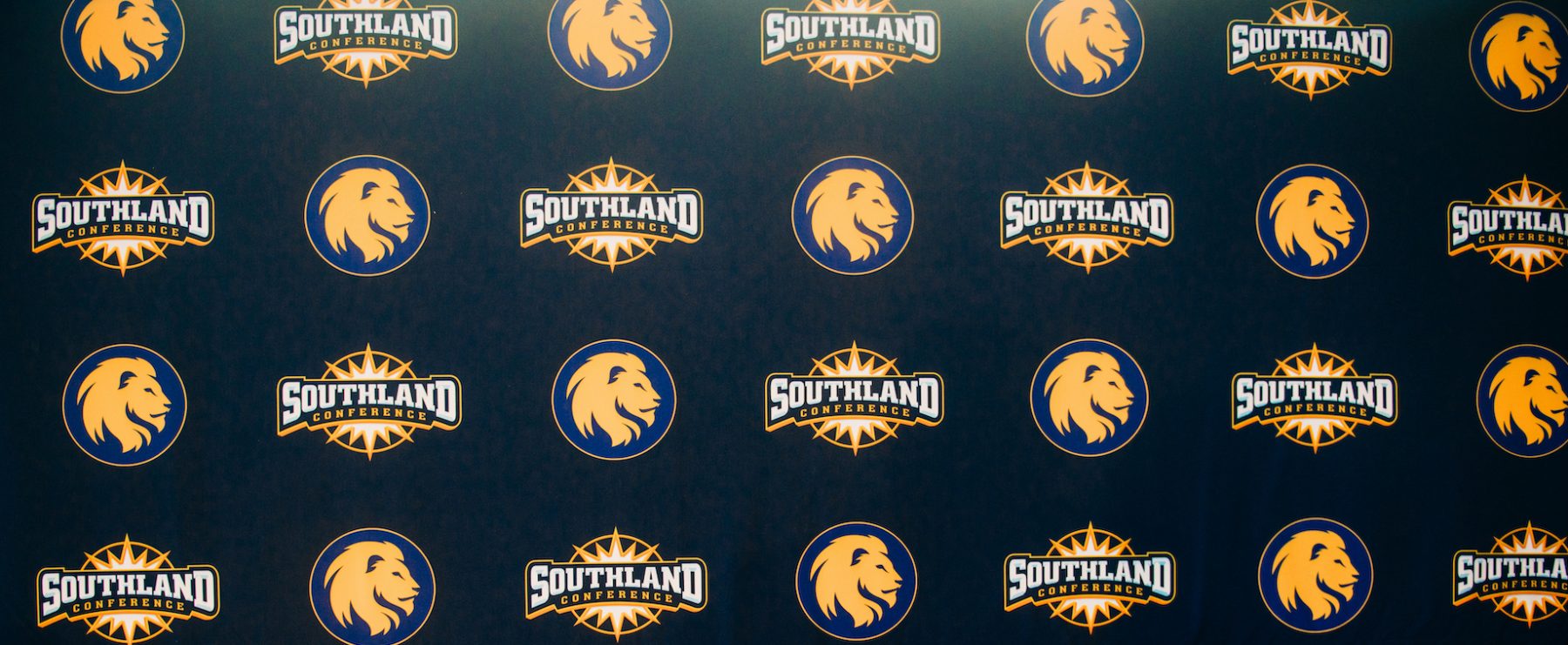 A decorative backdrop featuring the logos of A&M-Commerce and the Southland Conference