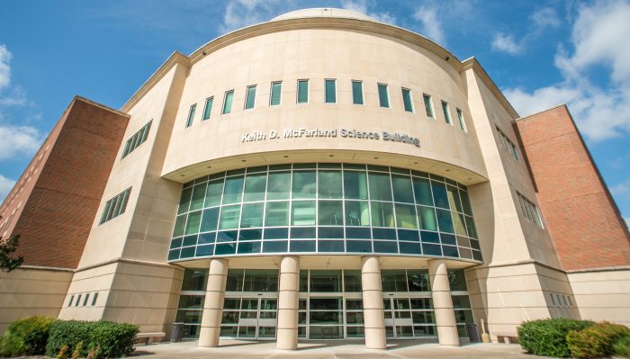 The image shows the Keith D. McFarland Science Building, featuring a modern facade with large glass windows and a rounded central structure.