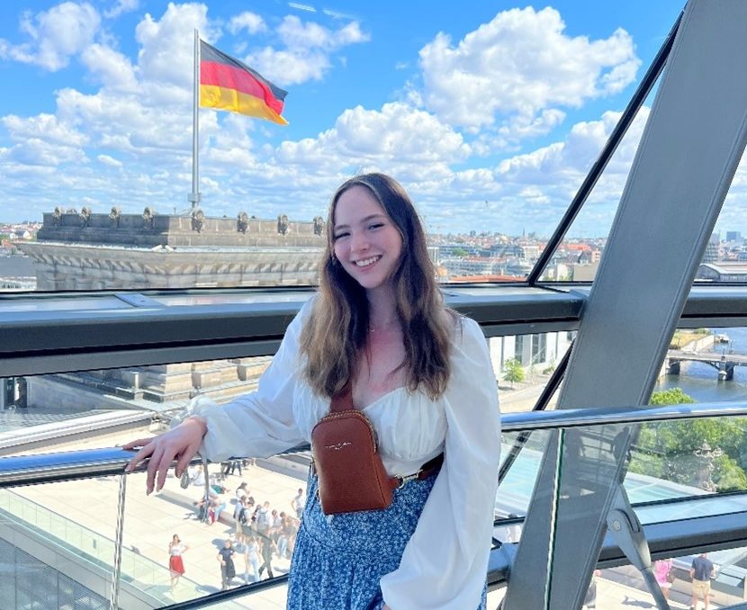 A young female in a glass bridge with a building behind her displaying the german flag.