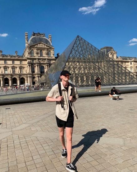 A young male in front of a glass pyramid in France.