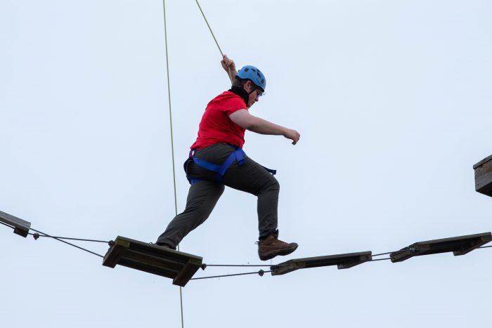 Person wearing red walking across logs on rope