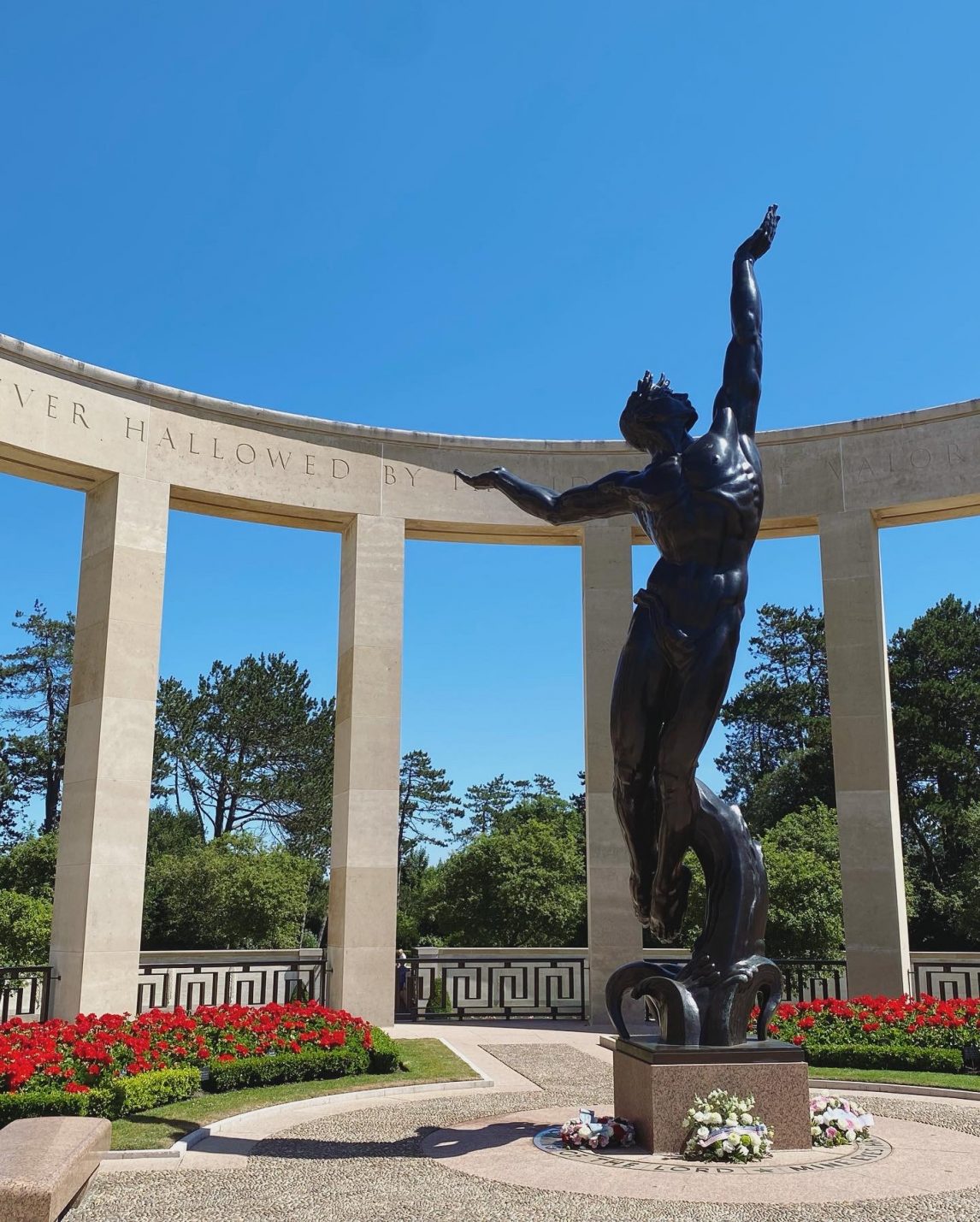 A picture of a male statue in front of a flower bed.