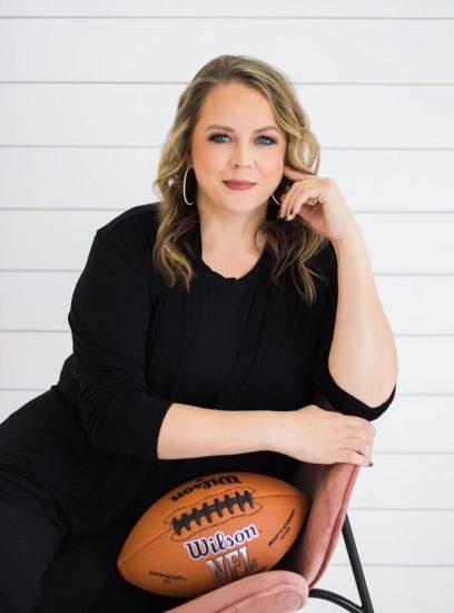 A woman looks at the viewer while leaning casually in a chair with a football