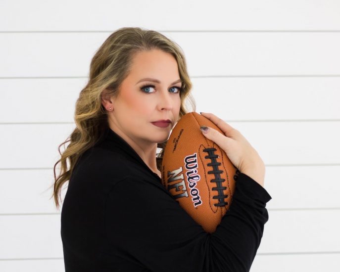 A woman poses with a football while looking at the viewer
