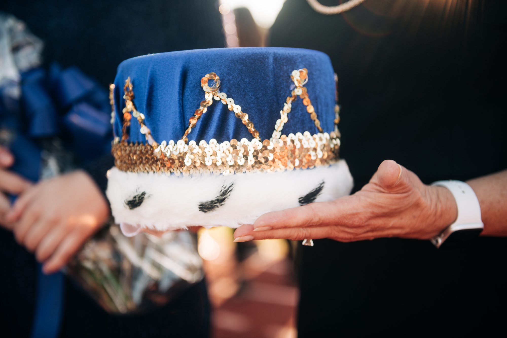 A pair of hands holding a blue, gold and white crown