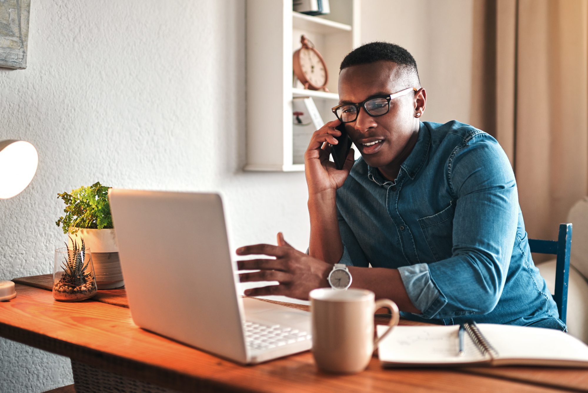 young businessman sitting alone in his home office and talking on his cellphone