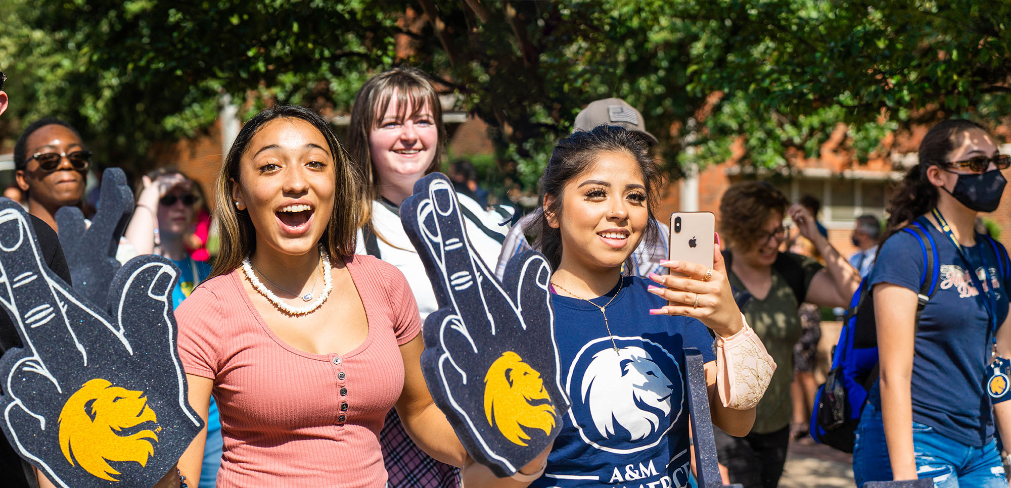 Three female students at the pride walk smiling at the camera with the leo sign. 