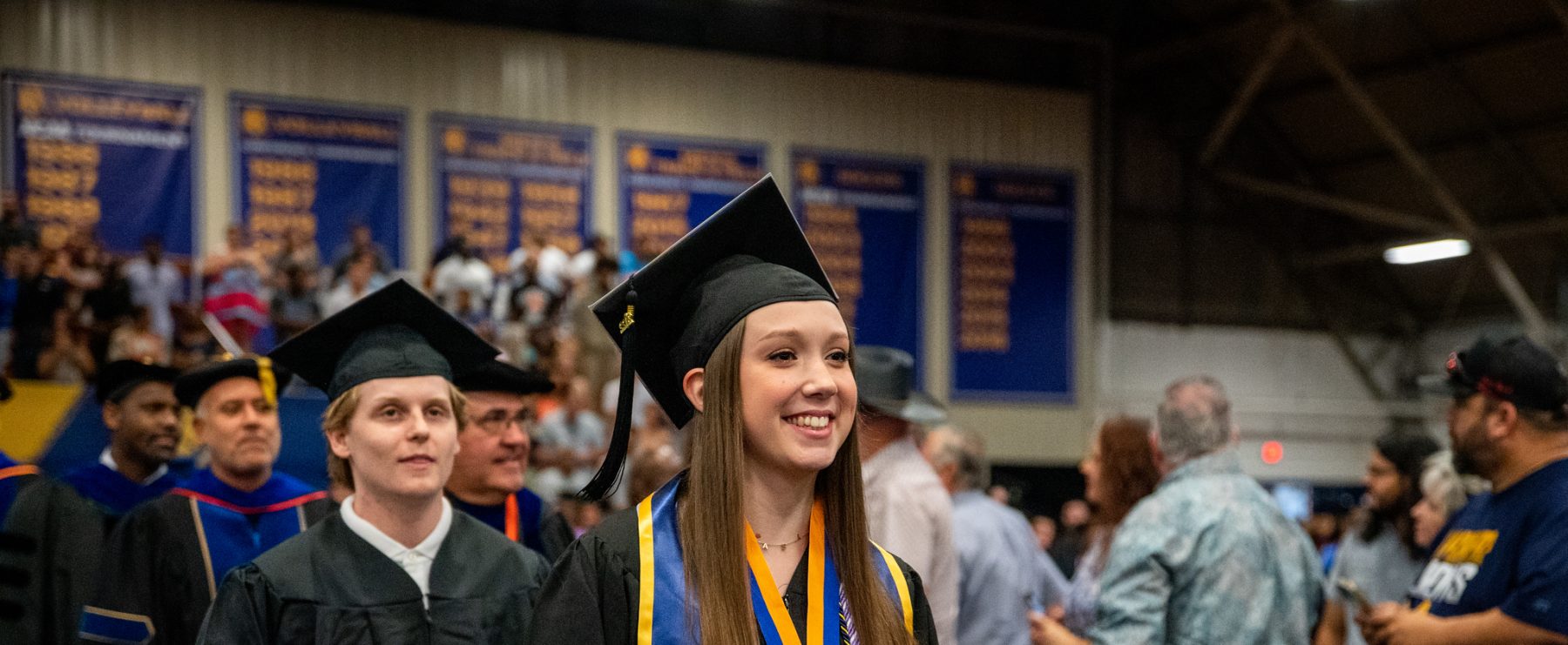 A female student smiling while walking down the aisle during graduating