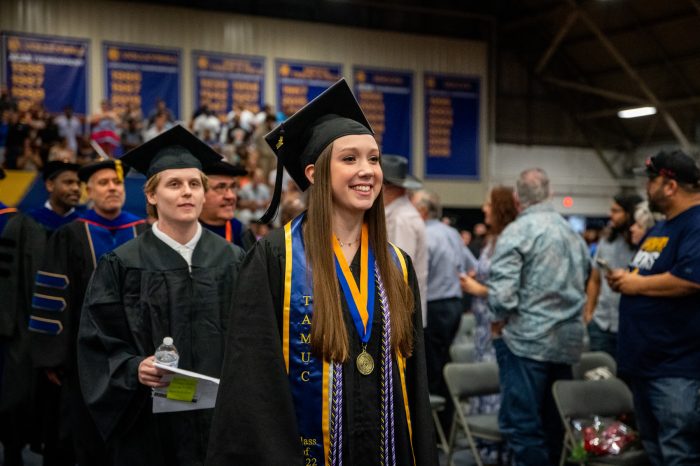 A female student smiling while walking down the aisle during graduating