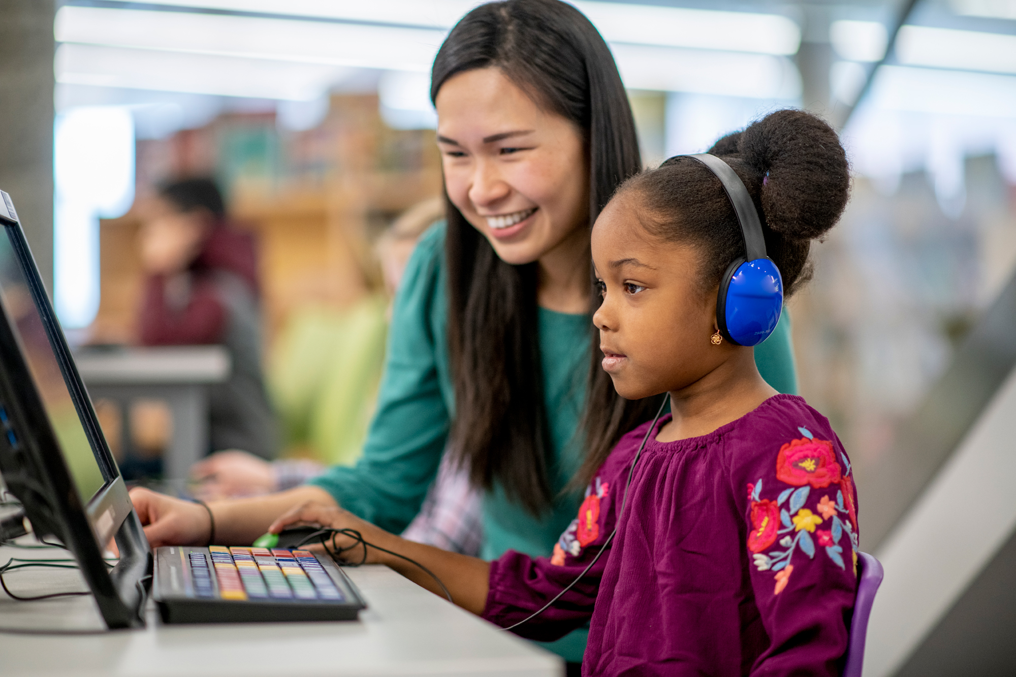 A female teaching student, helping a female enfant on the computer.