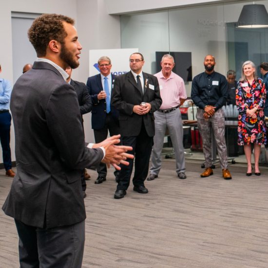 A group of people gather to listen to a person speaking.