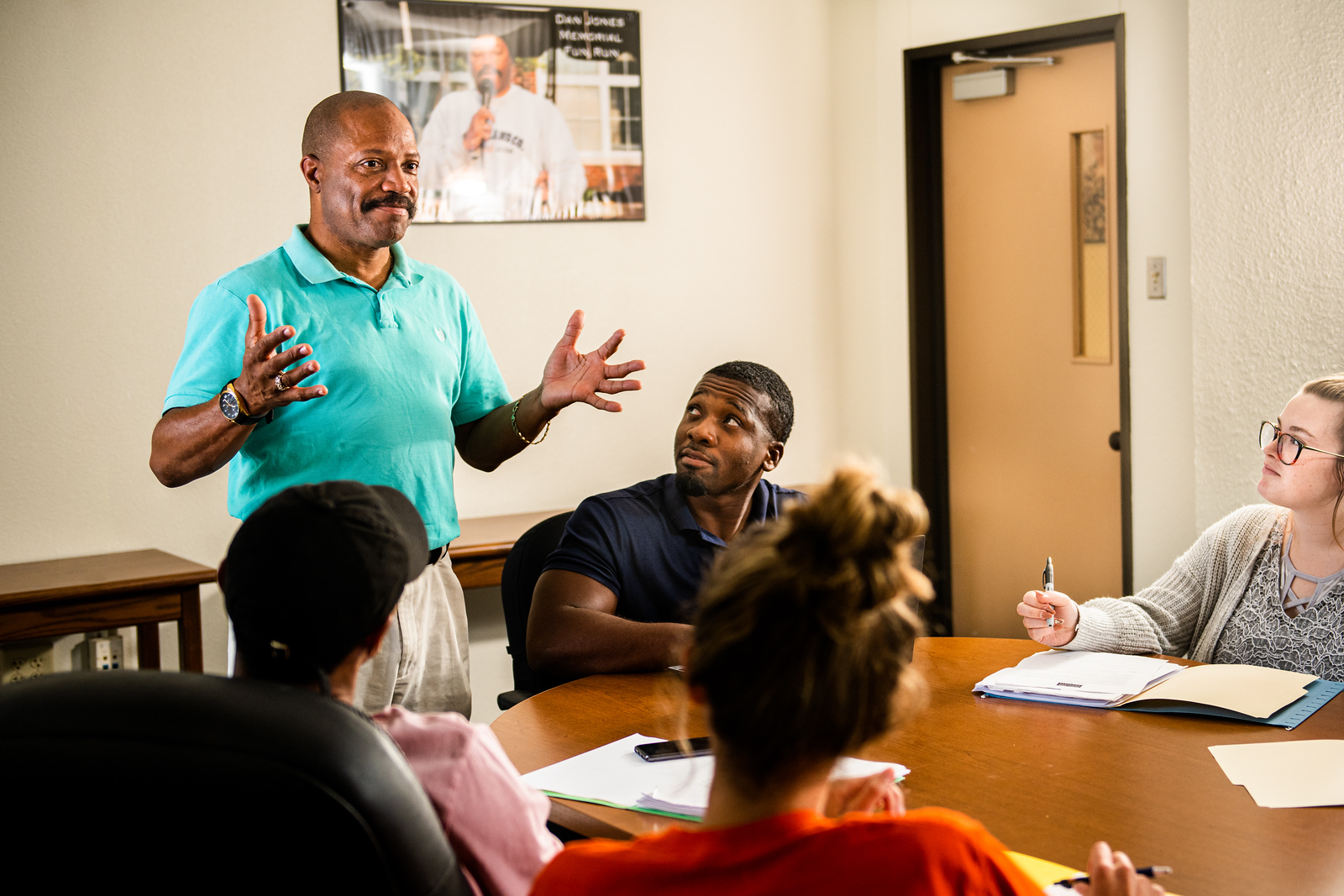 A black male professor teaching in front of students at a table.