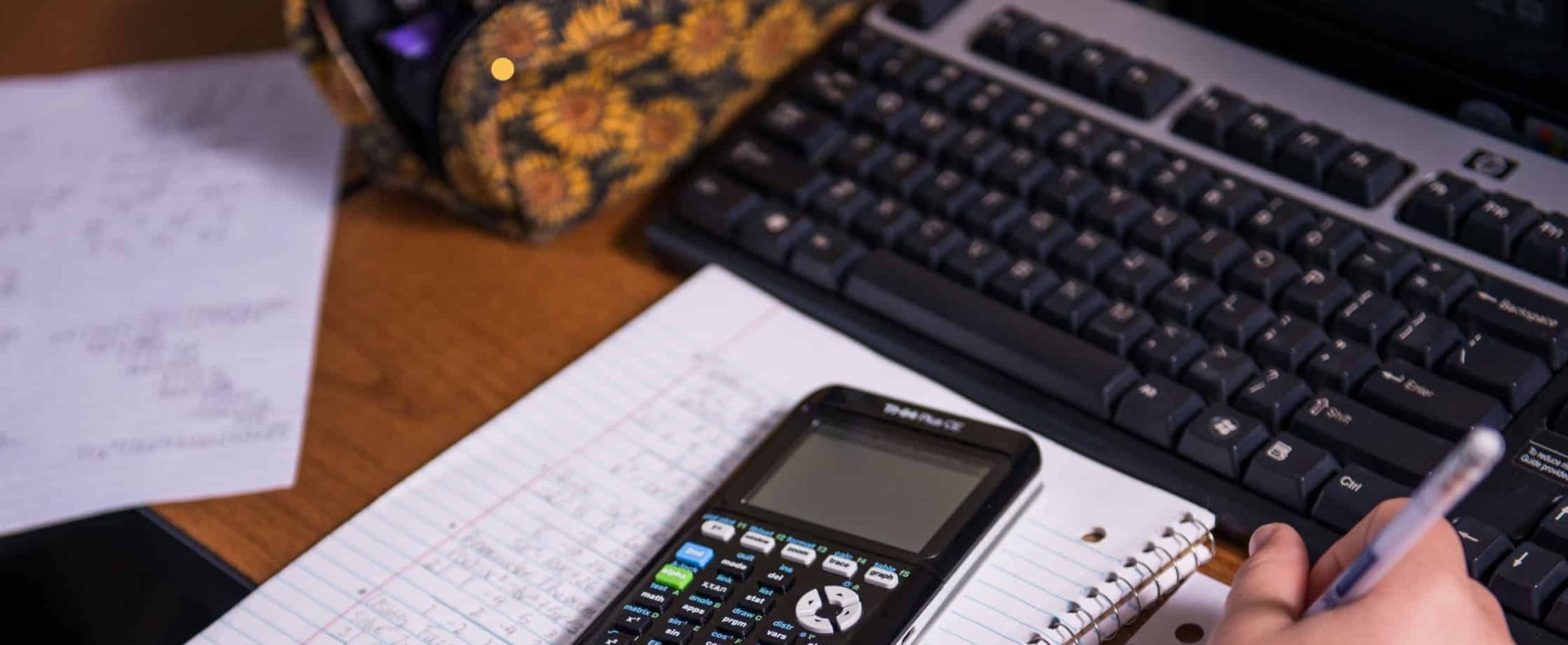 A calculator sits atop a spiral-bound notebook on a student's desk.