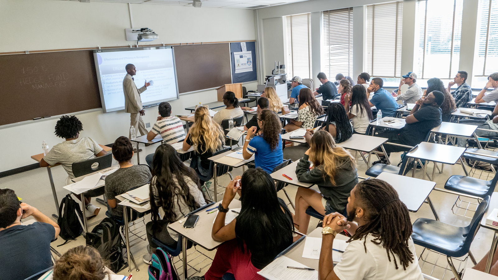 A group of university students in class while a male professor lectures.