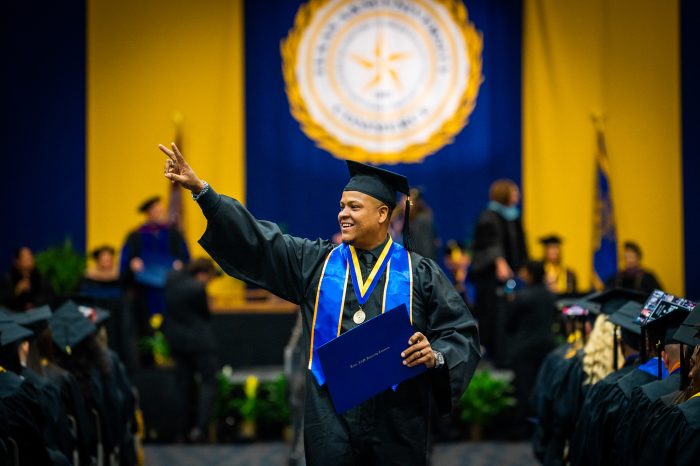 A&M-Commerce graduate extends arm and shows peace sign after receiving diploma.