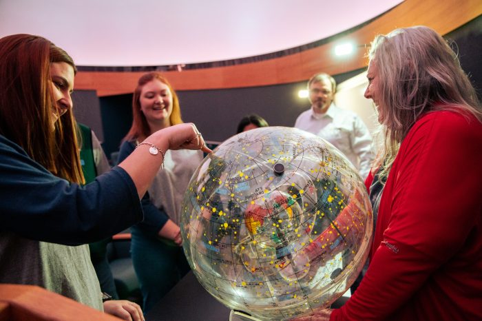 A group of females looking at an orb solar system.