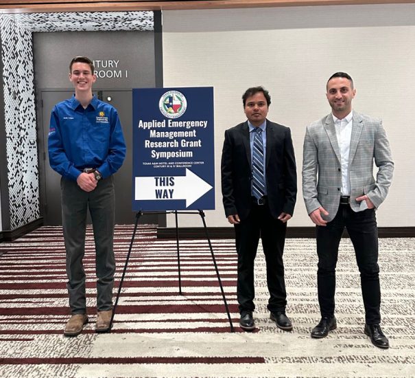 Three researchers stand next to a poster directing attendees.