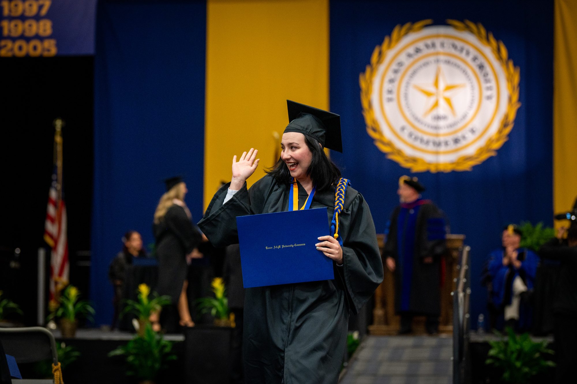 A female graduating student waging to the audience.