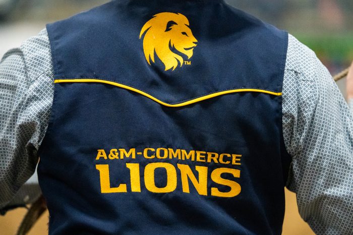 A person wearing a blue vest that reads "A&M-Commerce Lions" in gold stitching.