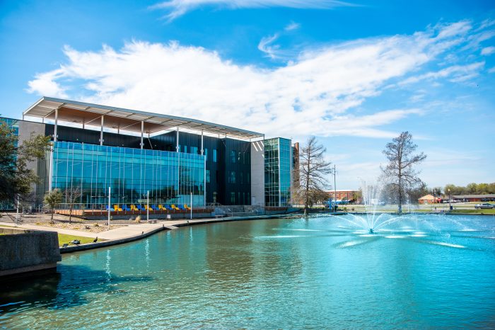 A photo of a glass building by the side of a lake.