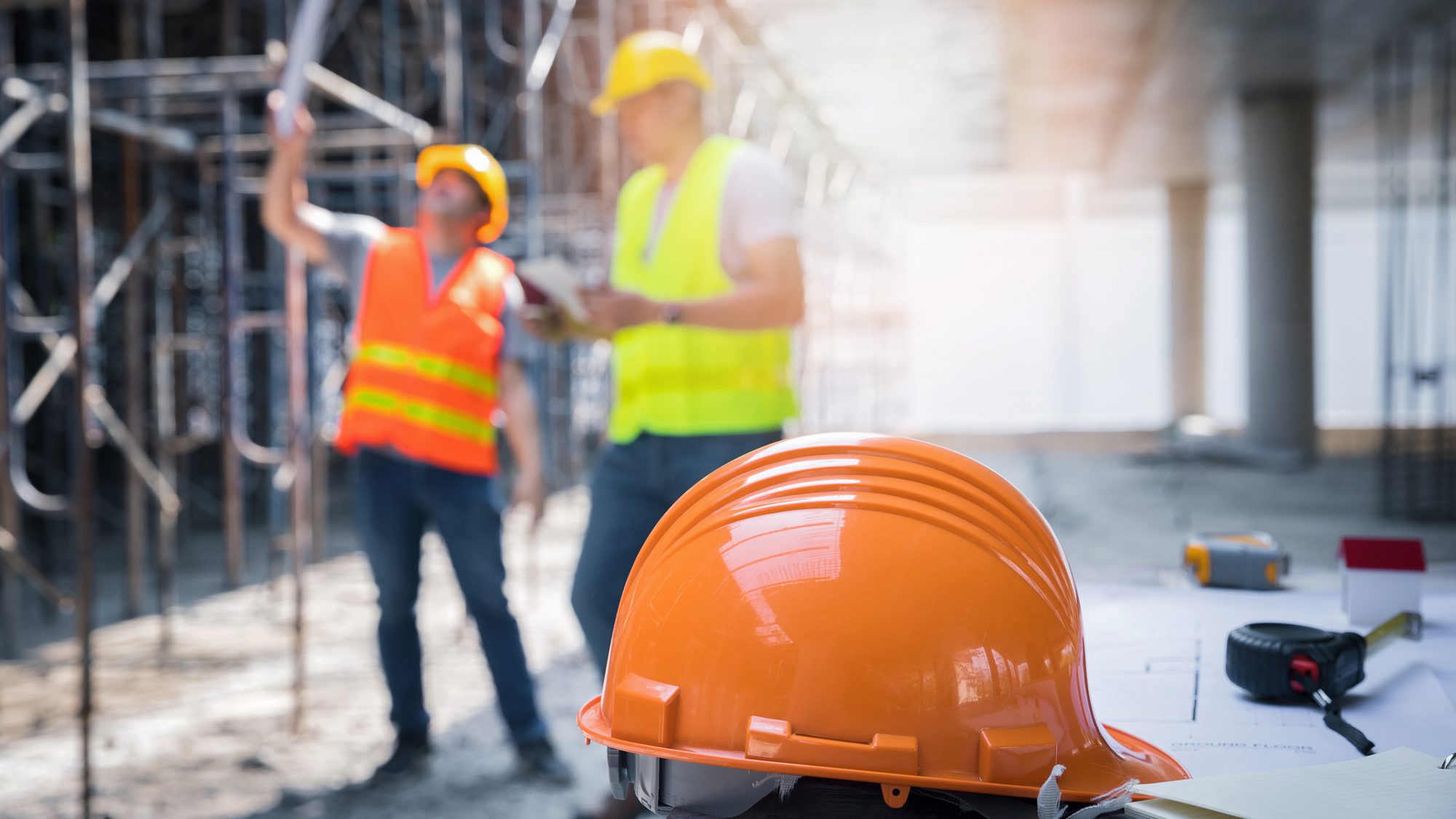 An orange helmet cap with two males looking at a plan. 