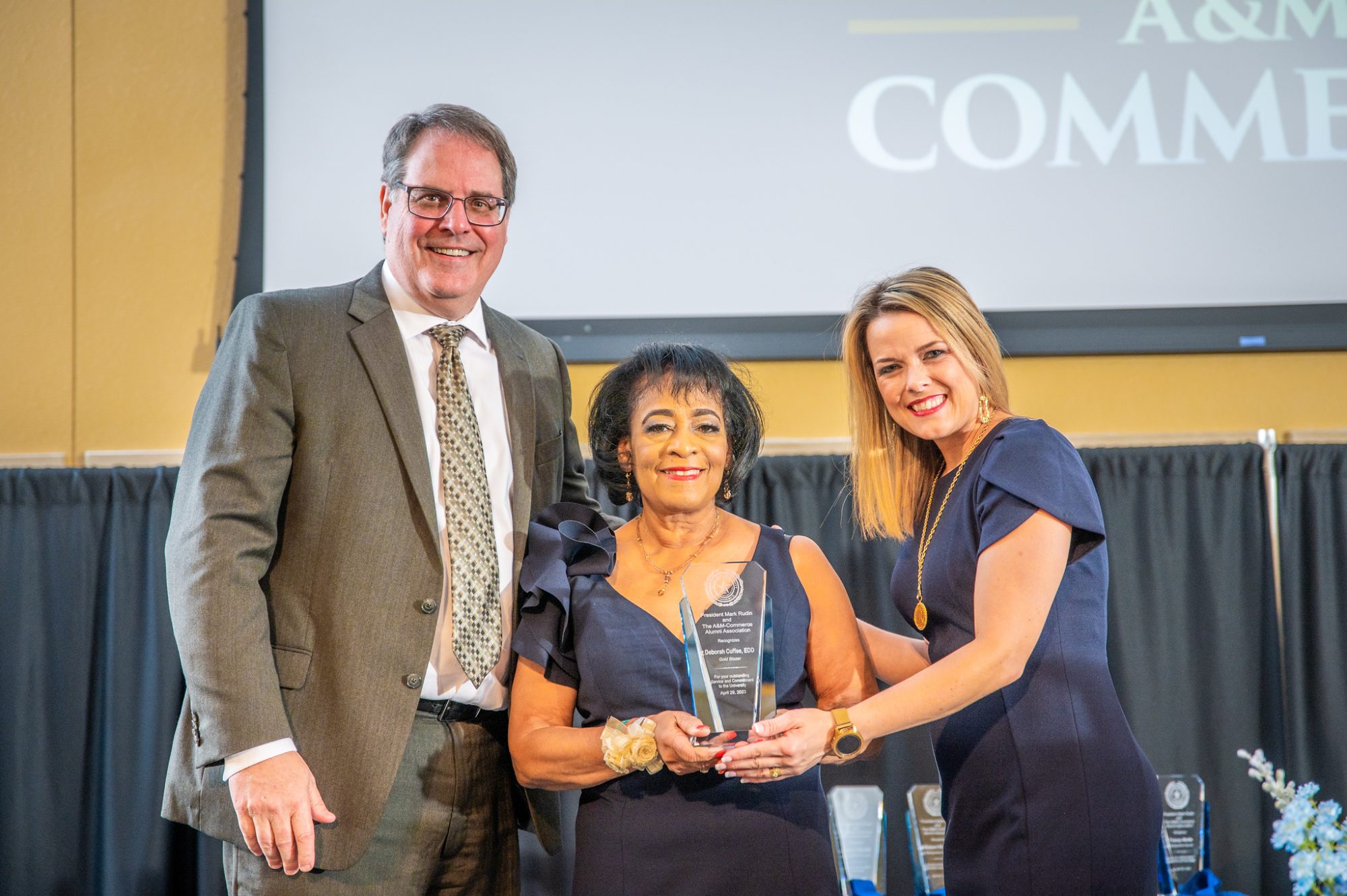 Awardee holds plaque alongside award presenters.