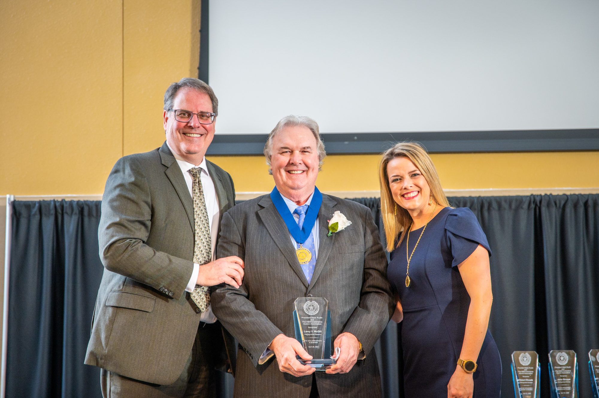 Awardee poses with award between two award presenters.