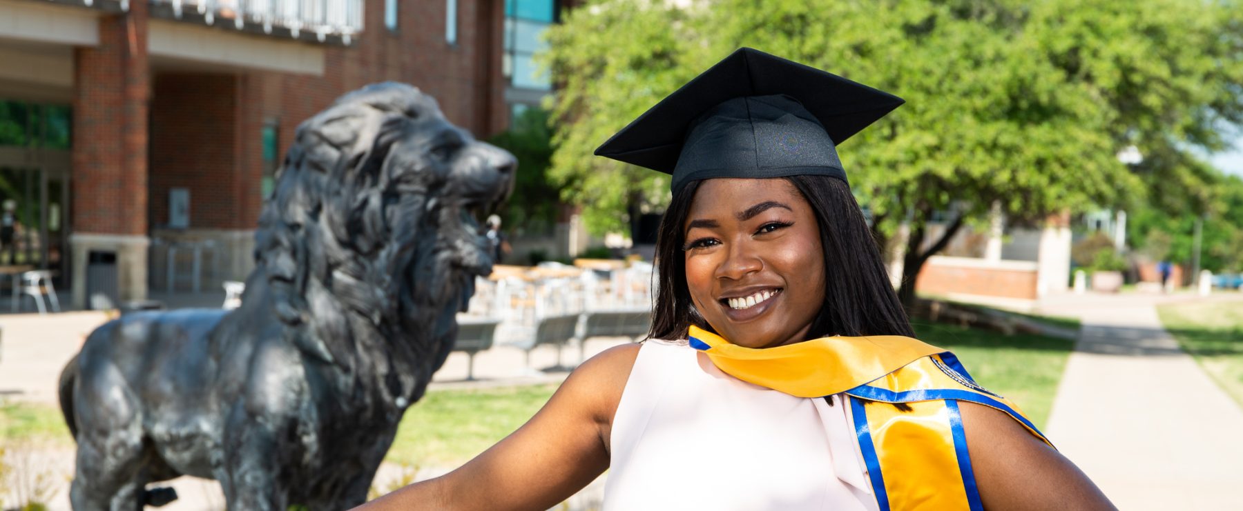 Graduate poses in graduation cap and stole with Lion statue in background.