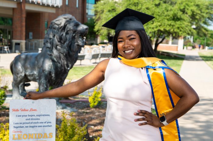 Graduate poses in graduation cap and stole with Lion statue in background.