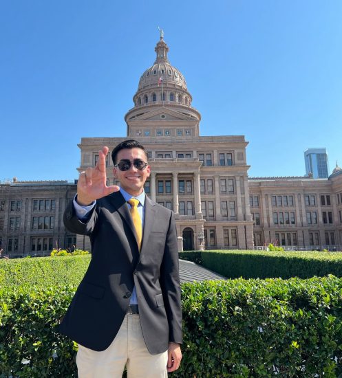 A person poses for a photo outside of a large government building.